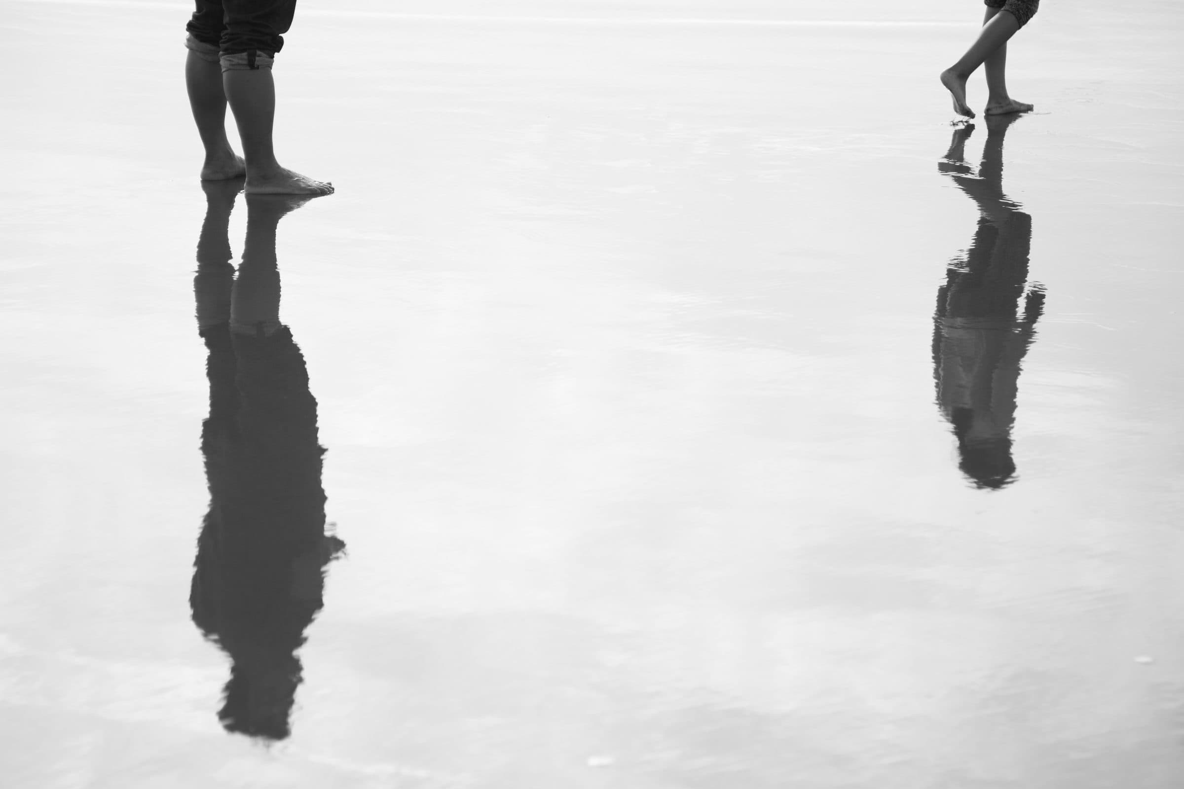 Black and white bare feet and their reflections on wet sand, fine art photograph by Jason Bowman