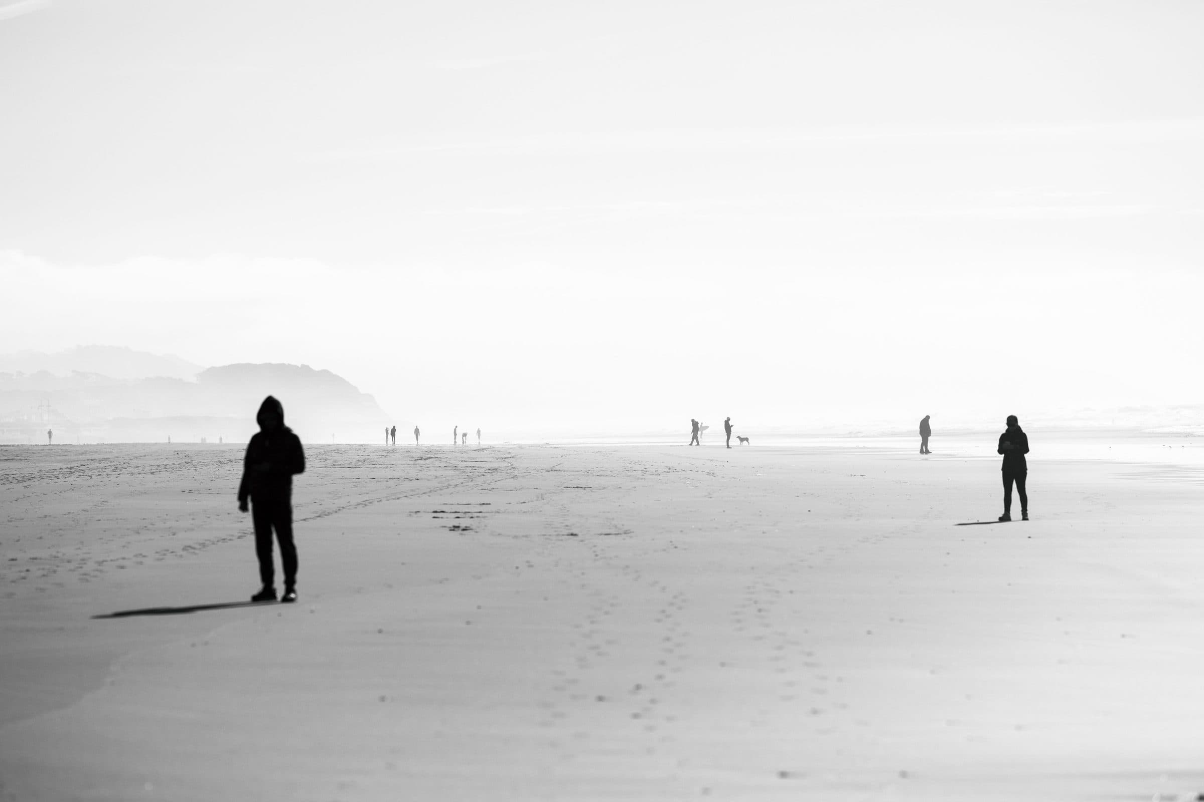 Black and white silhouettes of people on a hazy beach, fine art photograph by Jason Bowman