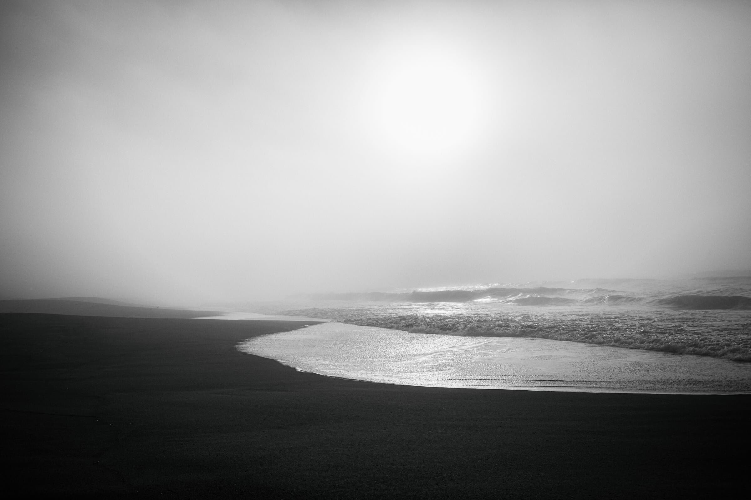 Black and white beach with sun breaking through fog, fine art photograph by Jason Bowman