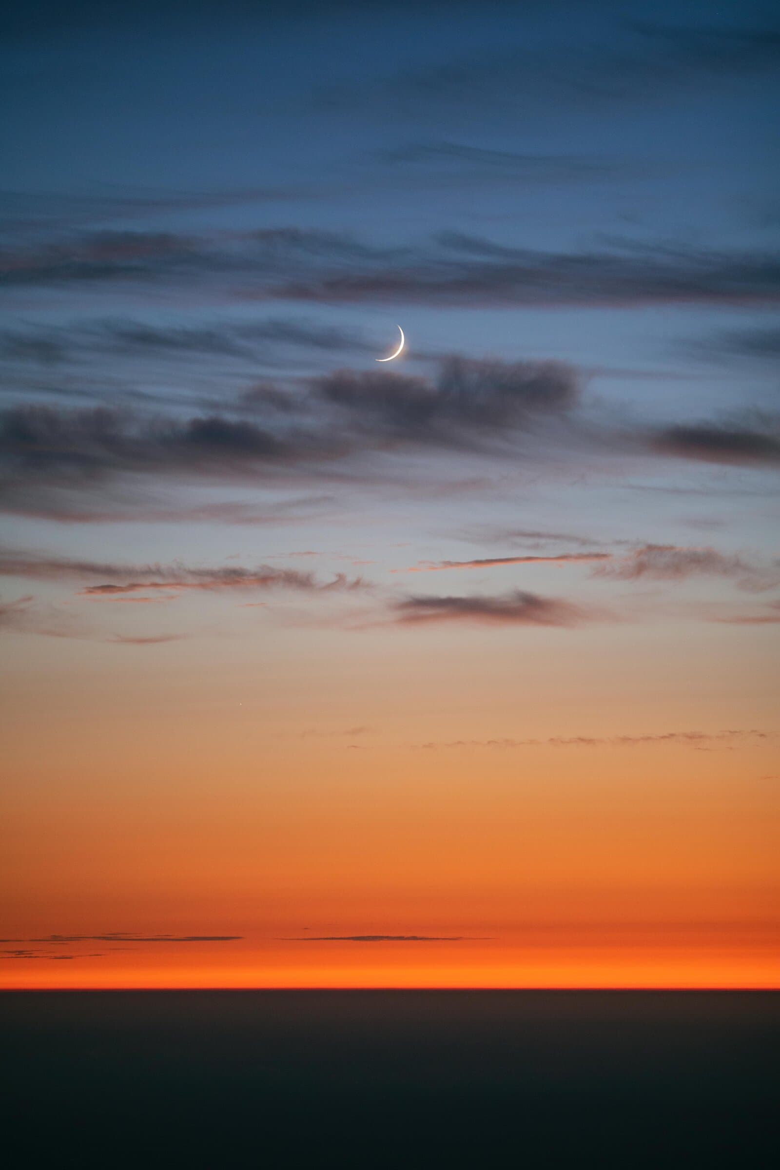 Crescent moon in a dusk sky over the ocean, fine art photograph by Jason Bowman