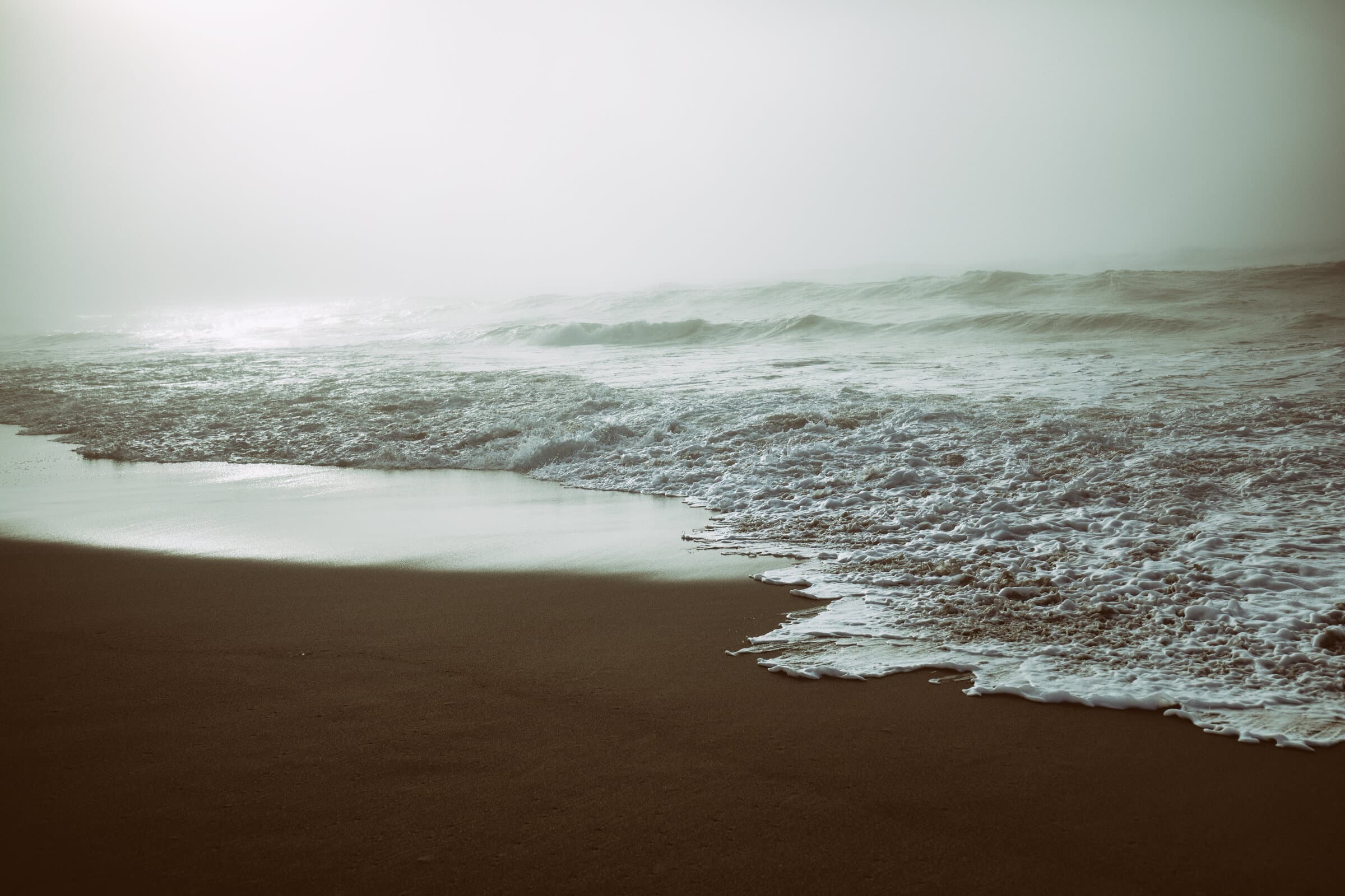 Foamy waves washing onto a dark beach in fog, fine art photograph by Jason Bowman
