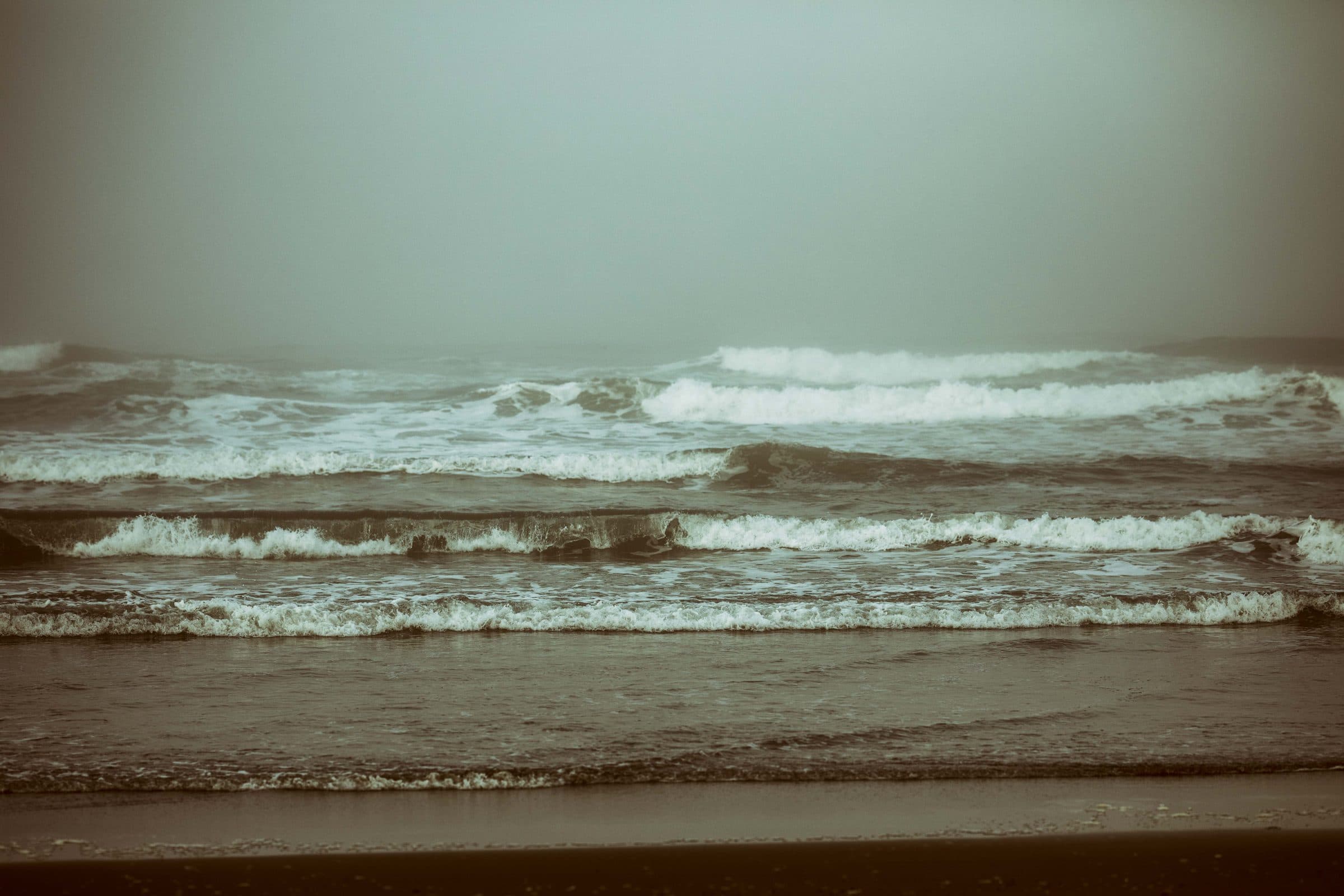 Rows of surf breaking in heavy fog, in muted tones, fine art photograph by Jason Bowman