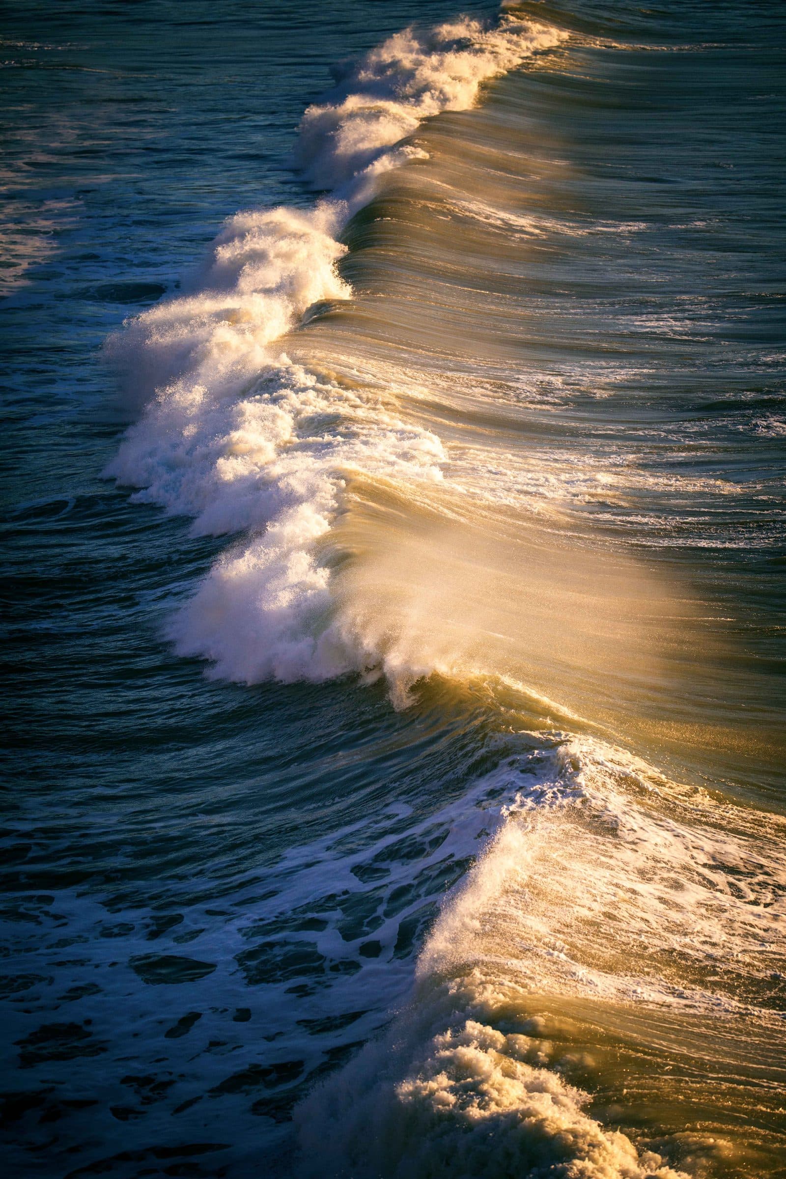 A breaking wave lit by golden light, fine art photograph by Jason Bowman