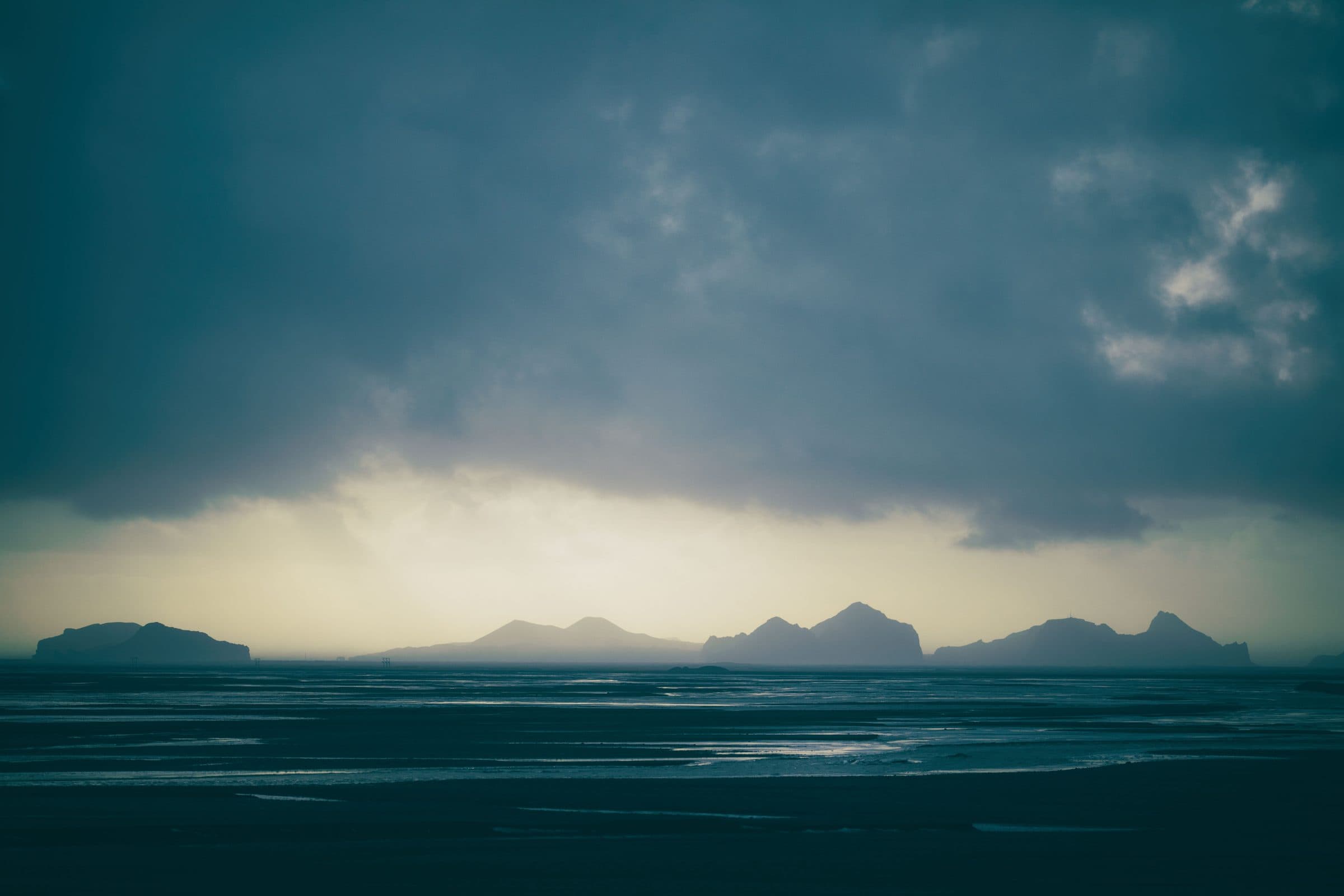 Island silhouettes under dark storm clouds beyond wet sand flats, fine art photograph by Jason Bowman