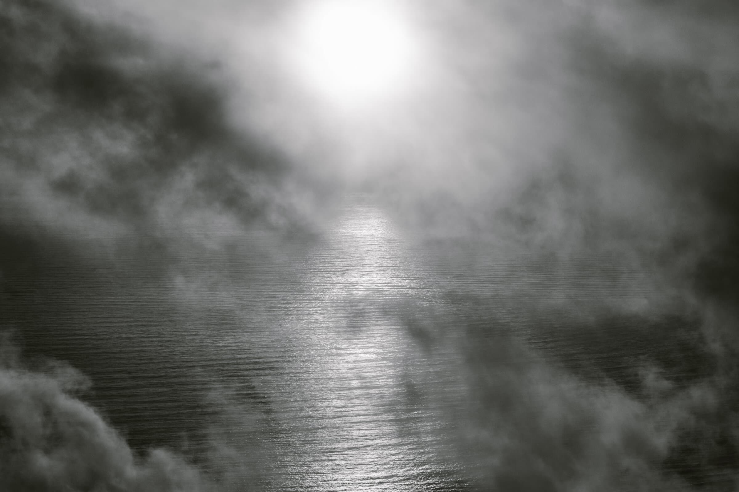 Black and white sun glowing through mist over water, fine art photograph by Jason Bowman