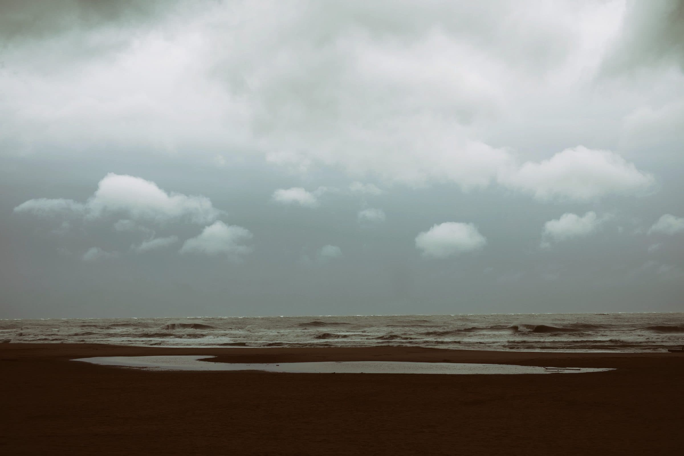 Stormy surf and a tide pool on a dark beach under clouds, fine art photograph by Jason Bowman