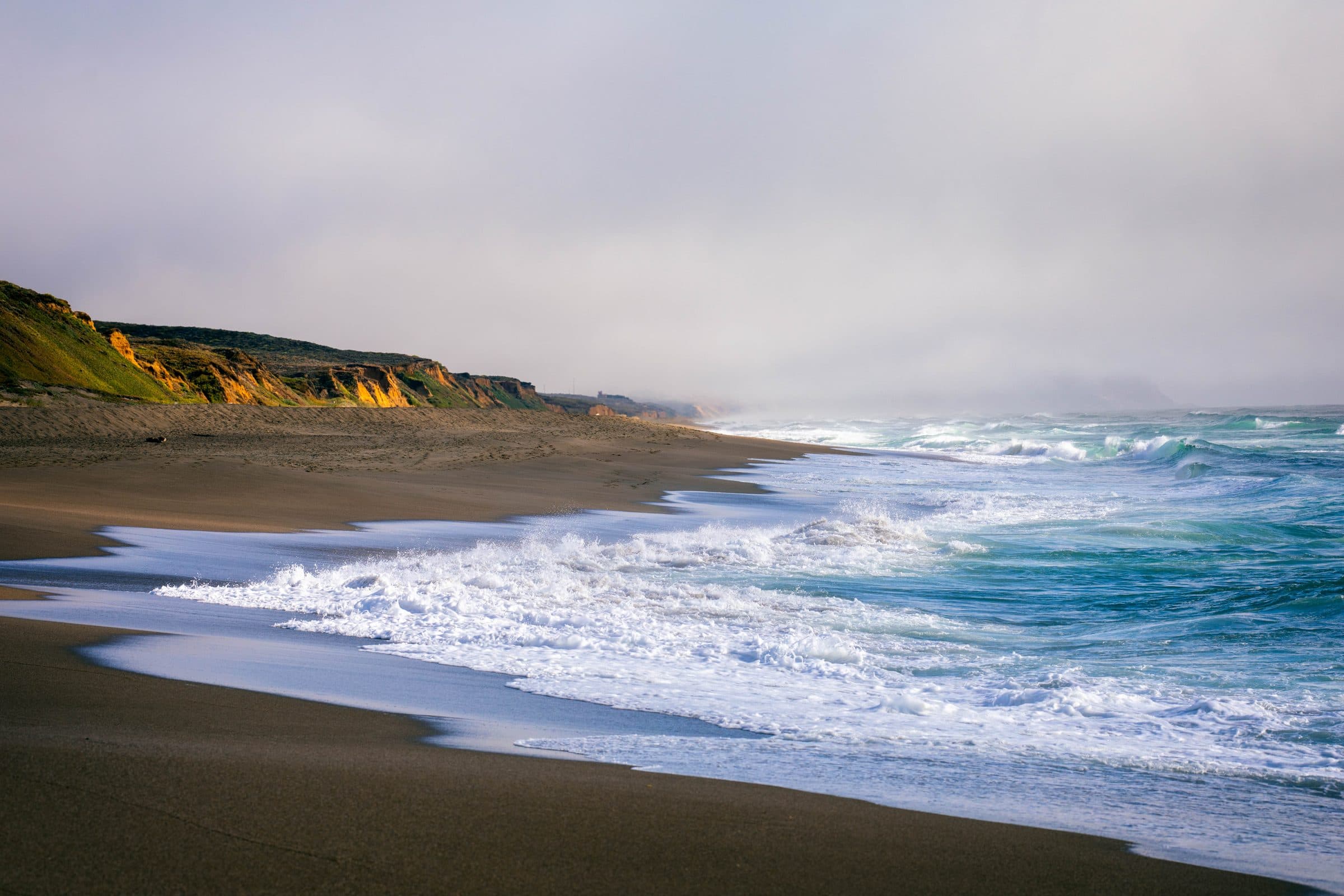 Sunlit coastal bluffs and surf fading into fog, fine art photograph by Jason Bowman
