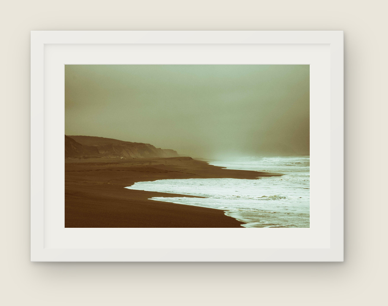 Framed photograph, sepia-toned beach cliffs and waves, in a white frame and mat hanging on a wall